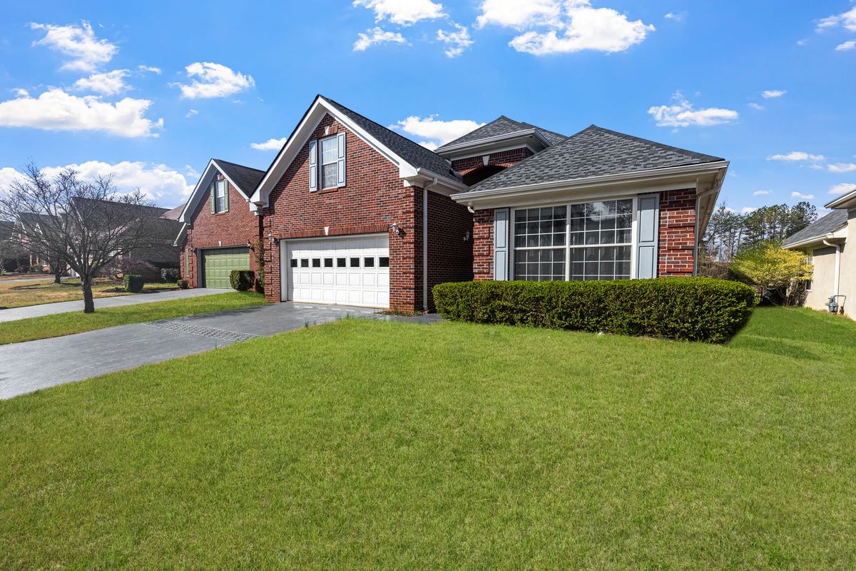 A red brick home with a white sectional garage door set back behind a long lawn