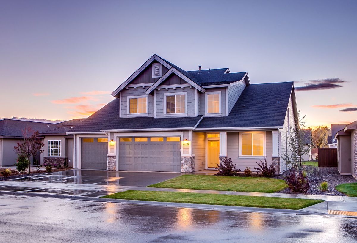 A two-storey home at dusk with lit windows and a wide sectional garage door, the street still wet after rain