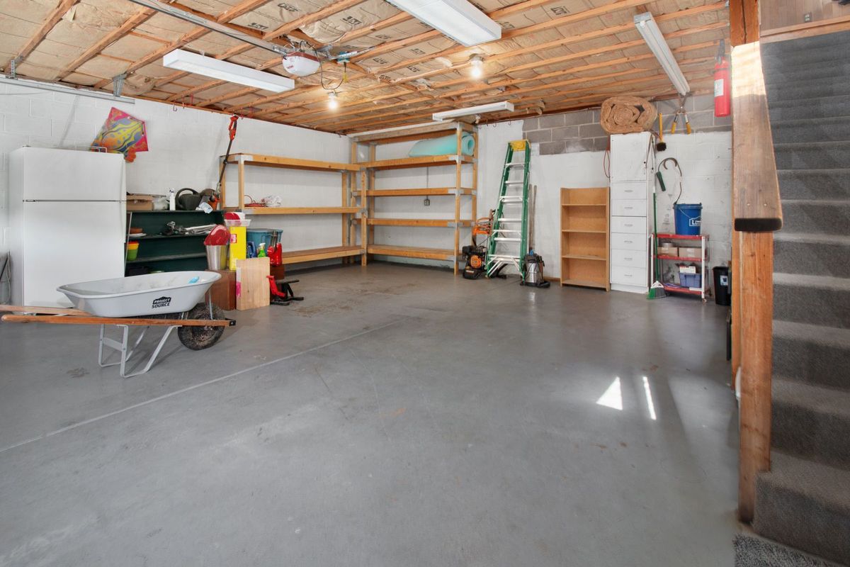 The inside of a tidy two-car garage with shelving, a ladder and a wheelbarrow