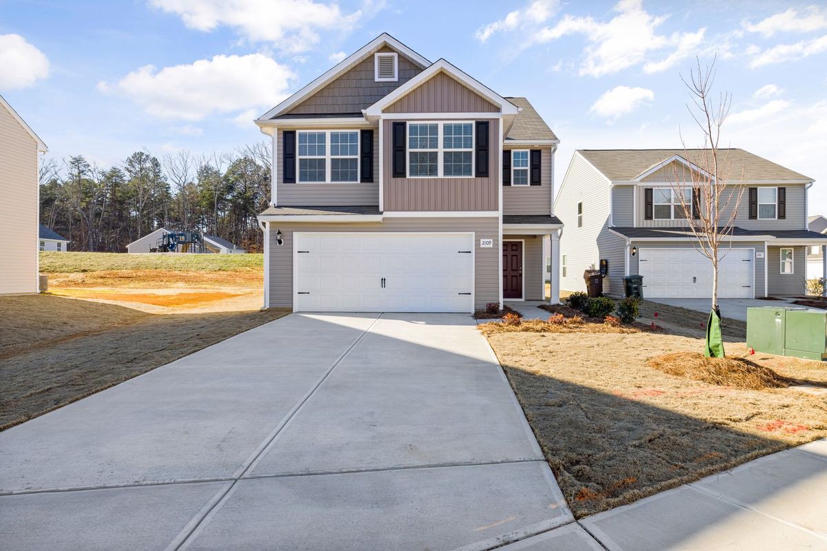 A new two-storey home in a growing subdivision with a white double garage door and a fresh concrete driveway