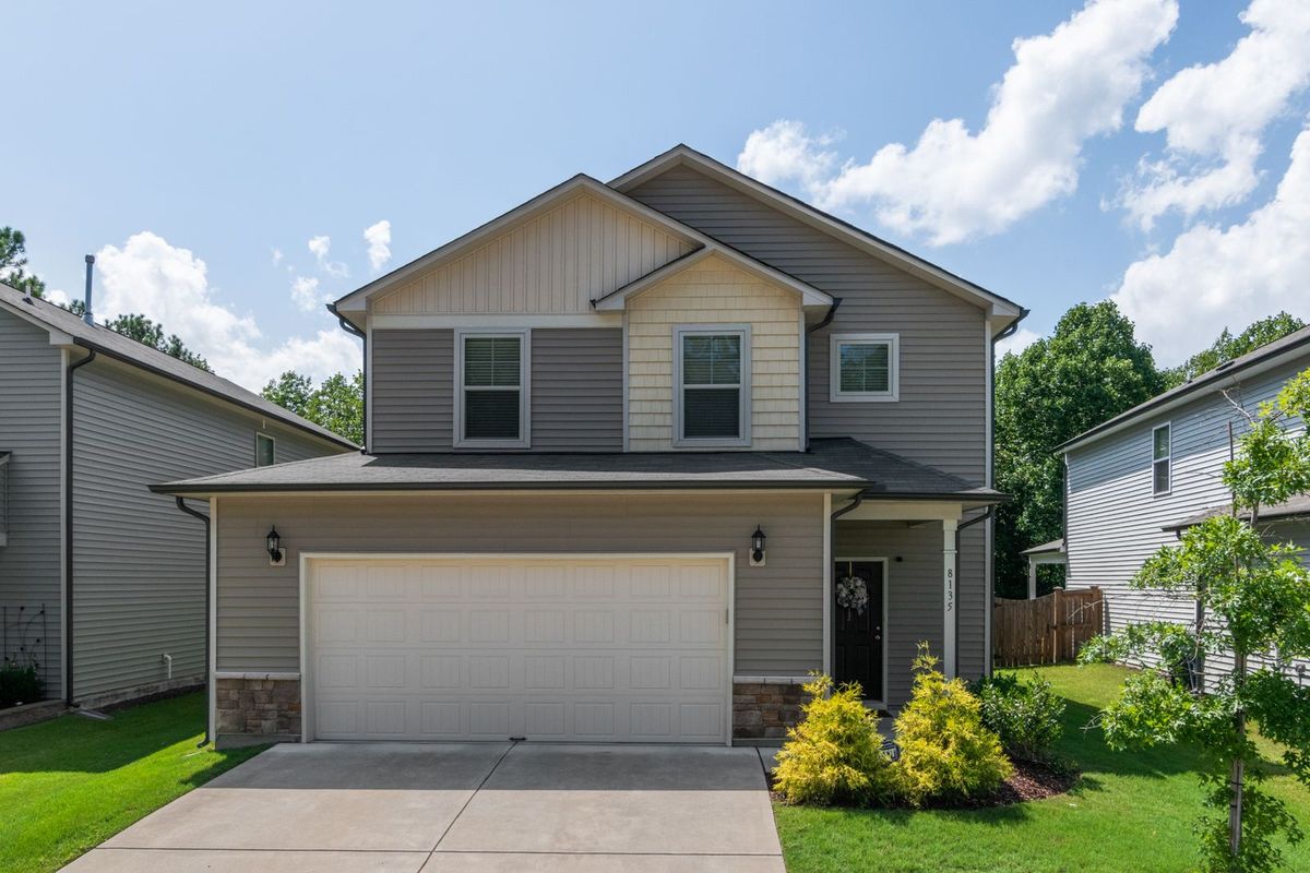 A two-storey home with a stone base and a white double garage door with window inserts