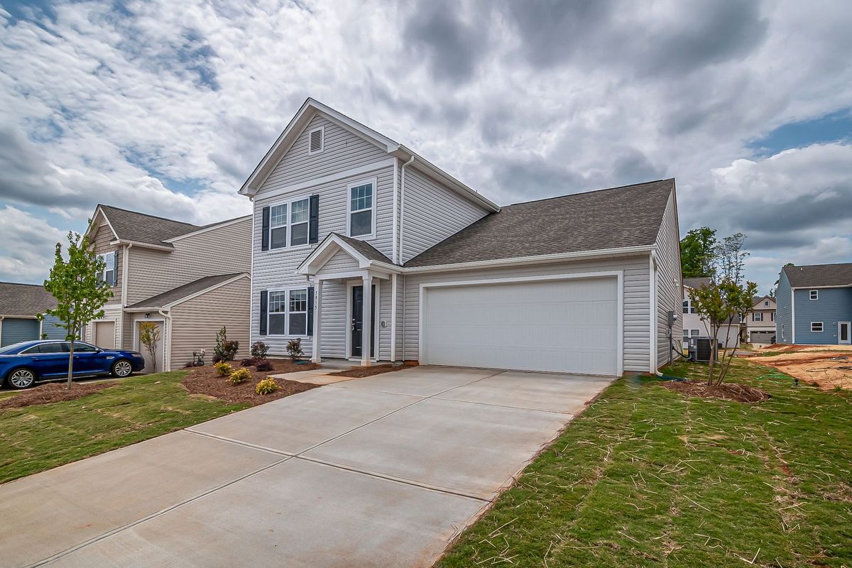 A two-storey home in a newer subdivision with a white double garage door and a long driveway